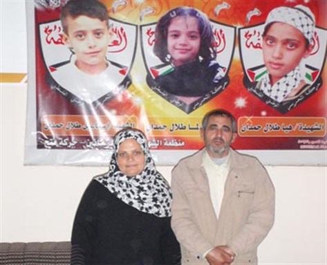 [Iman and Talal Hamdan standing in front of a picture of their killed children Hiya, Lama and Ismail. Image from PCHR.]