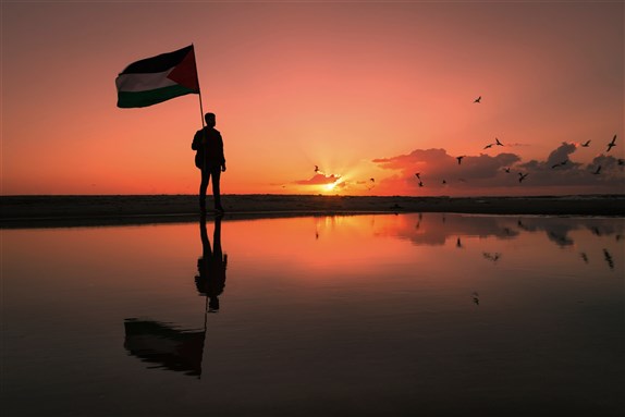 Youth holding up a Palestinian flag on Gaza beach, by Hazem Swidan via Shutterstock