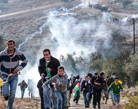 Bilin, Palestine, December 31, 2010: Palestinian protesters escape the tear gas during weekly demonstrations against Palestinian land confiscation and building Jewish settlement in Bilin. Image via Shutterstock.
