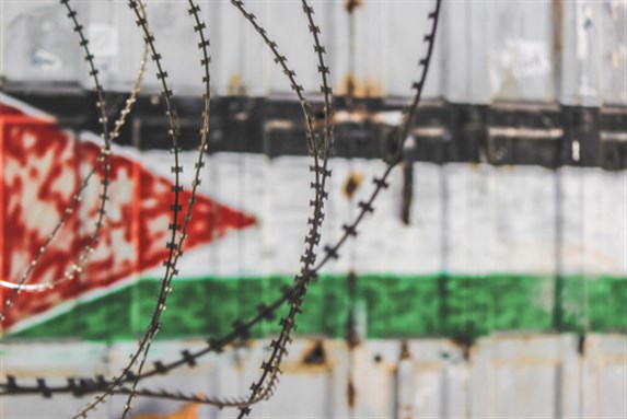 Palestine Flag through barbed wire in Old city of Hebron, Palestine. Image via Shutterstock.