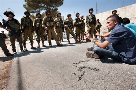 Palestinians in chains symbolizing solidarity with prisoners in Israeli jails face soldiers during a protest in Al Ma'sara, West Bank, 14 September 2012. Image via Shutterstock.