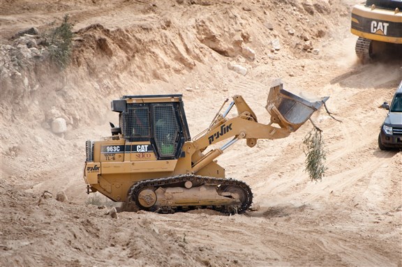 An olive branch hangs from a bulldozer clearing land for Israel's separation wall surrounding the West Bank town of Al-Walaja