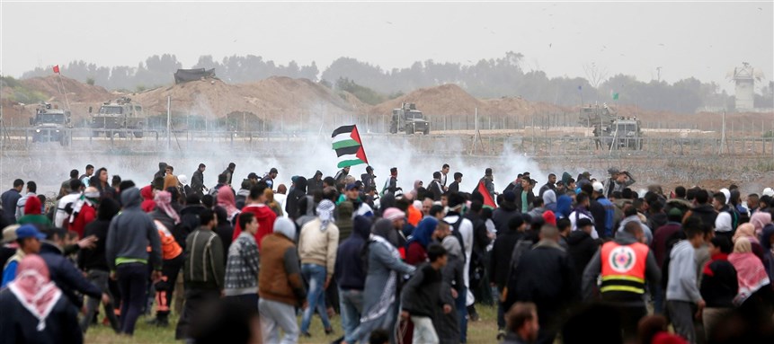 IMAGE:  Palestinian protesters run for cover as Israeli forces fire tear gas canisters during clashes following a demonstration marking the first anniversary of the “March of Return” protests, near the border with Israel east of Gaza City on March 30, 2019.  (Photo by MAHMUD HAMS/AFP via Getty Images)