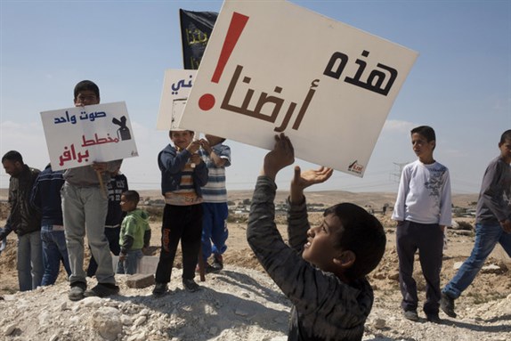 [A boy displays a sign that reads “This is our land!” during a vigil to mark Land Day in the unrecognized Bedouin village of Wadi al-Naam in present-day Israel, 30 March 2012. Bedouins in the southern Naqab region have resisted decades of ongoing, forced displacement by Israeli authorities. Image by Keren Manor via ActiveStills]