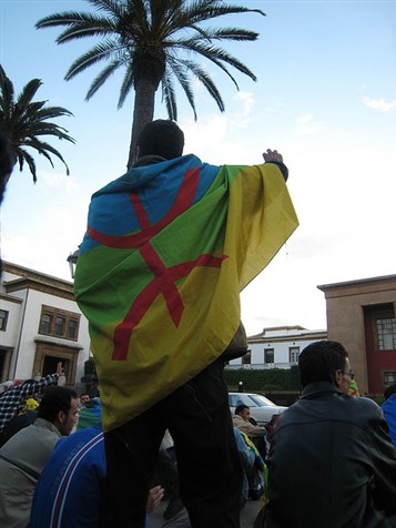[A protester carrying the Amazigh flag during a demonstration in front of Morocco`s parliament. Image from Carlyjoy86 on Flickr.]