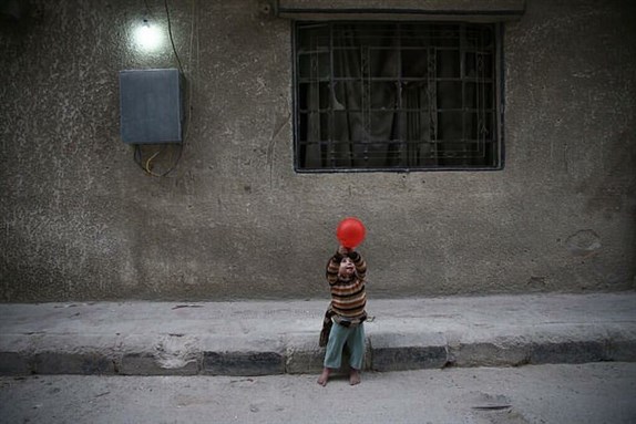 [Image of a Syrian child standing in Aleppo with a simple red balloon. Image by Hasan Almossa via flickr]