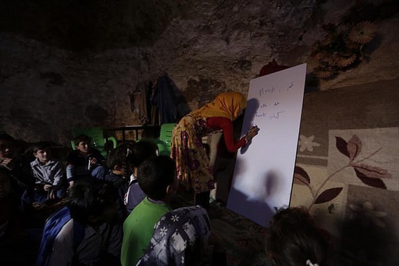 [Image of a teacher conducting a lesson for internally displaced children inside a cave in Tramla, in indlib province, Syria. Image by Khalil Ashawi via Flickr)