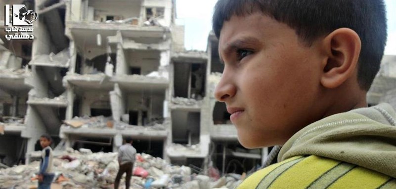 [A young Syrian looks over destroyed housing in Sabqa, Damascus. Via Lens Young Dimashqi.]