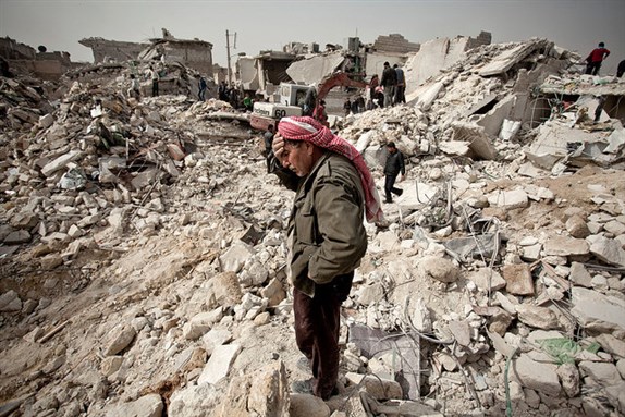 [A Syrian man reacts while standing on the rubble of his house while others look for survivors and bodies in the Tariq al-Bab district. Image by Nic6192131 via Flickr]