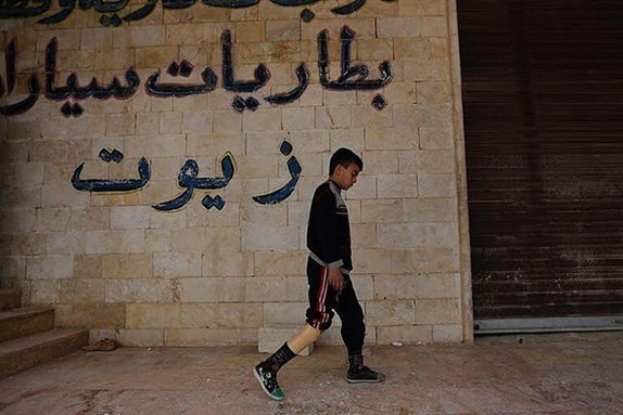 [Image of a boy walking with his artificial limb in rebel-held Maaret al-Numan, Syria. Image by Khalil Ashawi via Flickr]