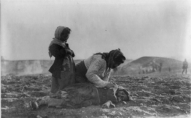 [An Armenian woman kneels beside a dead child lying in a field in Syria. Image from Wikimedia Commons.]