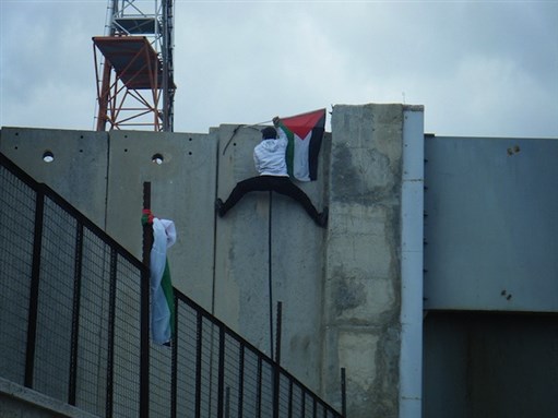 [Protestor puts flag on top of separation wall in Bethlehem on Land Day, 2012. Image by Palestine Solidarity Project via Flickr.]