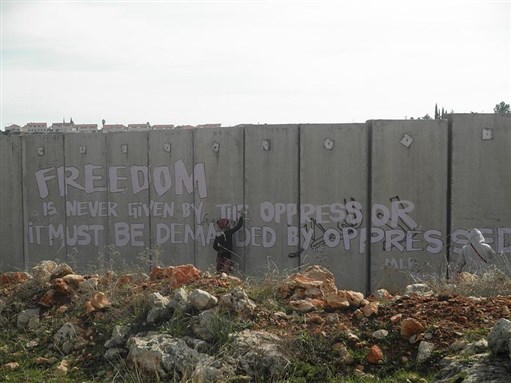 [International Solidarity Movement activists writing graffiti on the separation wall, Ni`lin. Image by Yoram Sorek, via Wikimedia Commons.]