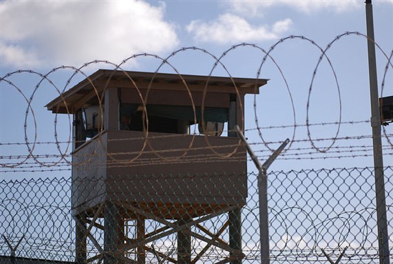 [A Soldier stands guard in a tower at Camp Delta at Joint Task Force Guantanamo Bay. Image by Spc. Cody Black. From Wikimedia Commons.] 