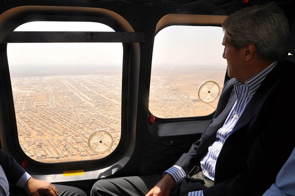 [U.S. Secretary of State John Kerry views the Mrajeeb al-Fhood camp for Syrian refugees as he flies back to Amman, Jordan, from visiting the nearby Za`atri refugee camp on July 18, 2013. Image from US Department of State / Public Domain]