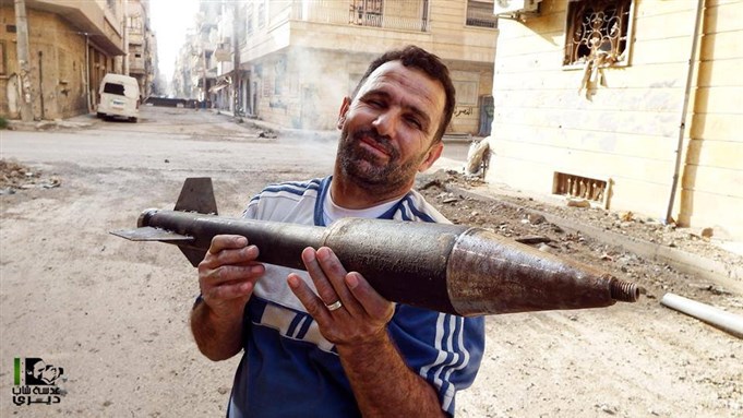 [A man displays an unexploded rocket which had fallen in Al-Ordi. Deir Ezzor, 19 May 2013. From Lens of a Young Deri.]
