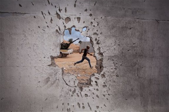 [A Libyan revolutionary fighter runs for cover while attacking pro-Gadhafi forces in Sirte, Libya, October 2011. AP Photo/Manu Brabo]