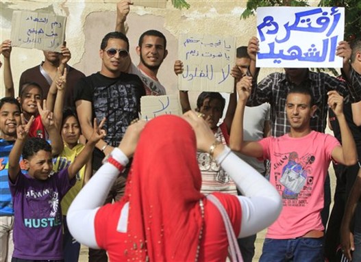 [Egyptians flash Arabic signs \"no for feloul-- or `remnants` of the regime, center, \"remember martyrs blood\", right, and \"we will not waste martyrs blood,\" left, outside a polling station as the wait for the arrival of presidential candidate Ahmed Shafiq, a former Air Force commander and civil aviation minister whom Mubarak made prime minister during his last days in power, May 23, 2012. Image by Amr Nabil/AP Photo.]