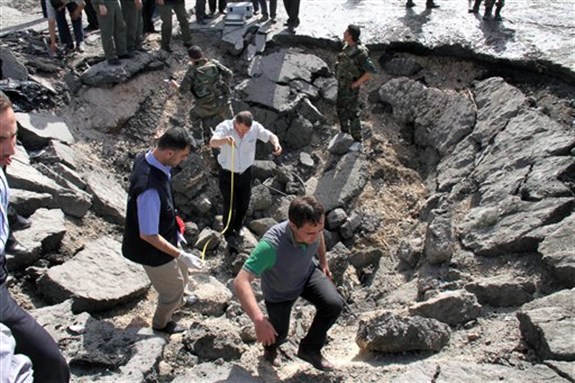 [Syrian inspectors investigate the crater in front of a damaged military intelligence building where two bombs exploded, Qazaz neighborhood, Damascus, Syria, May 10, 2012. Image by Bassem Tellawi/AP Photo]