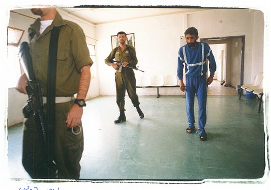 [Israeli guards escort a shackled prisoner. Image by Miki Kartzman for Physicians for Human Rights – Israel]