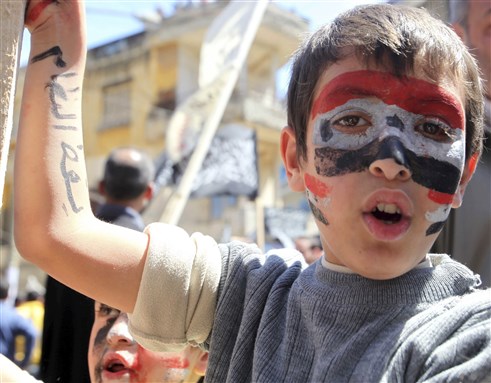 [A Syrian boy at a protest. \"Down with the Regime\" is written on his arm. Image from Unknown Archive]