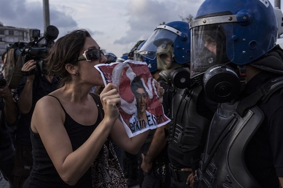 [People gathered for the press statement of Berkin Elvan’s family at Taksim Square, confronted by riot police. Berkin Elvan is a fourteen-year-old boy who was shot in the head with a teargas capsule when he went out to buy bread on 15 June 2013; he has been in a coma since then. Image by Erhan Arik / Nar Photos.]