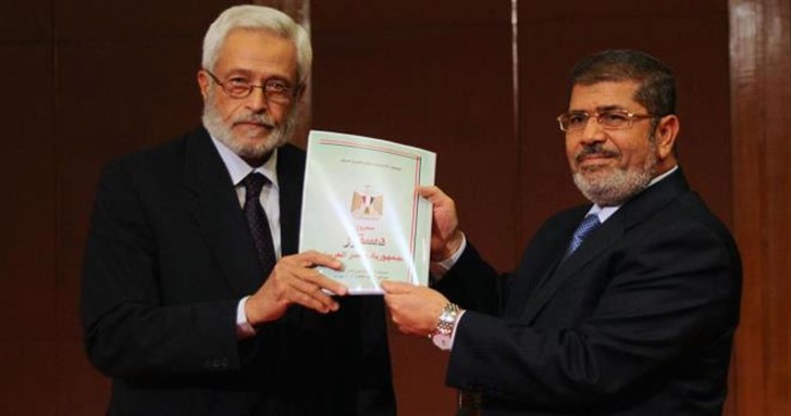 [President Mohamed Morsi and Head of the Constituent Assembly Hossam al-Gheriany hold a copy of the draft constitution. Photo from President Mohamed Morsi`s official Facebook page.]