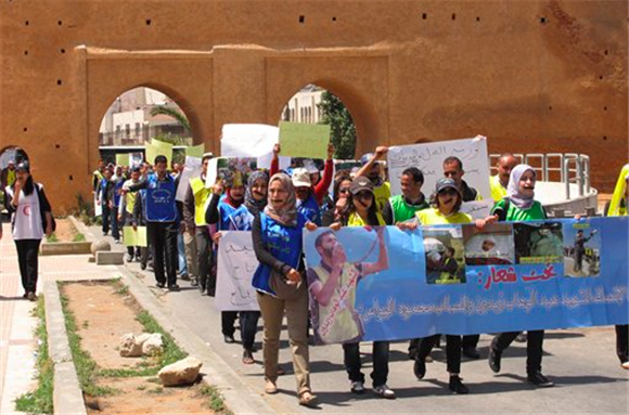 [Young unemployed university graduates, some with their mouths taped over, carrying out a silent march through the ancient city walls of the Moroccan capital Rabat on April 26, 2012 with images of an unemployed man who set himself on fire to protest the lack of jobs. Image by Paul Schemm/AP Photo.]
