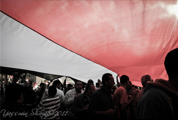 [Protestors in Tahrir Square under an Egyptian flag, Cairo, Egypt. Image originally posted to Flicker by Yass Sharaf] 