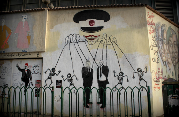 [1 June 2012, graffiti during the presidential elections showing Shafiq and Morsi as poppets controlled by a general (the joker). Image originally posted to Flickr by Gigi Ibrahim]