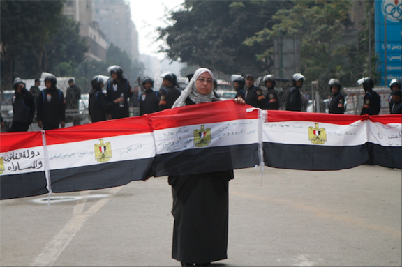 [23 January 2012, woman holds flag in protest calling for equality, implementation of civil law, and the end of military trials of civilians. Image originally posted to Flickr by Sarah Carr] 