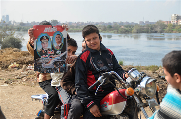 [14 January 2014, children holding poster advocating for a “yes” vote on the constitution. The Arabic reads: “Yes to the great constitution of Egypt.” Image originally posted to Flickr by camilo g. r.]