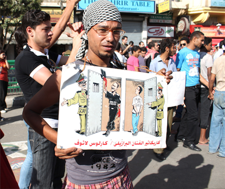 [23 July 2011, protester holding a poster drawn by Brazilian political cartoonist Carlos Latuff. Image originally appeared on Flickr by Nora Shalaby.] 