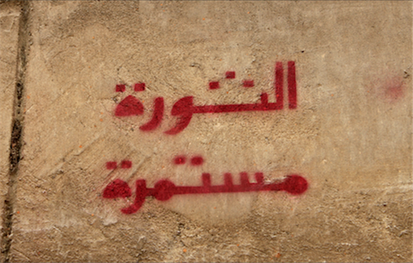 [\"The Revolution Continues\" graffiti in Arabic on Abdel Salam Aref Street. Image originally posted to Flickr by Nora Shalaby.]