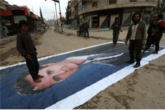 [Fighters from a coalition of Islamist forces stand on a portrait of Syrian President Bashar al-Assad in Idlib, Syria. Image by Zein Al-Rifai via AFP]