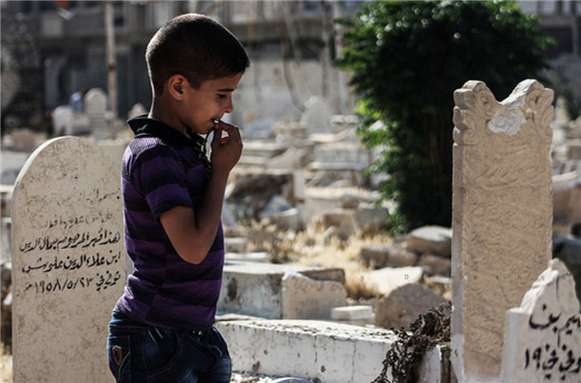 [Image of a Syrian child standing in front of his father`s grave on the first day of Eid al-Fitr. Image by Dimashqi Lens via Flickr]