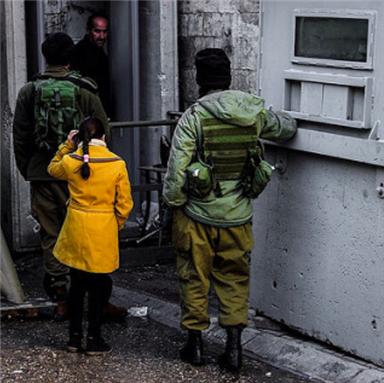 A Palestinian girl watches as her father is checked by fully armed Israeli soldiers as he passes one of the many checkpoints of occupation in Hebron. Israeli forces continue the policy of checking nearly everyone that passes through. Photo taken by CPT Palestine and uploaded form Flickr