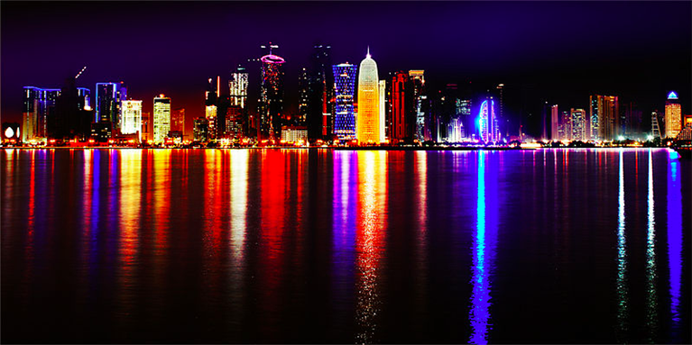 [Doha, Qatar. Skyline at night. Showing the expansion of the business district. Photo taken by Nuroptics and uploaded via Wikimedia Common]