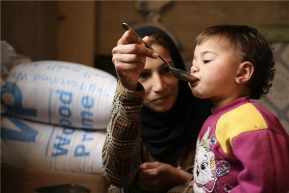 Woman displaced with her family from Douma in rural Damascus to Adra - feeding her 18 month old daughter lunch via World Food Programme by Abeer Etefa