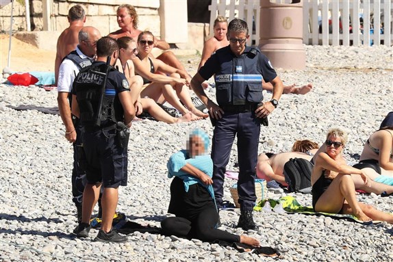 [Armed police in Nice forced a woman on a beach to remove her burkini, sparking outrage online. Image from Vantage News]