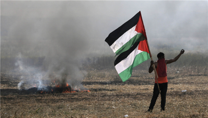 A protester holding Palestinian flags gestures during protest at Gaza border (photo by Reuters, March 2018).
