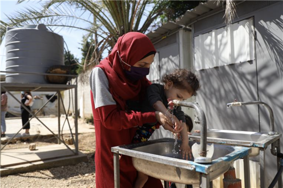 Mother Kanouz holding her one-year old daughter Fatima to wash her hands at Mhamara informal settlement, 5 July 2021 via UNICEF