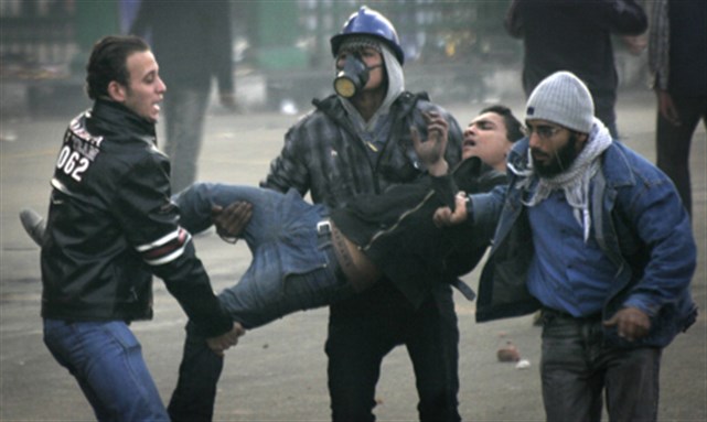 [Egyptian protesters carry an injured fellow protester during clashes with military police near Tahrir Square in Cairo, Egypt Saturday, 17 December 2011. Image from AP]