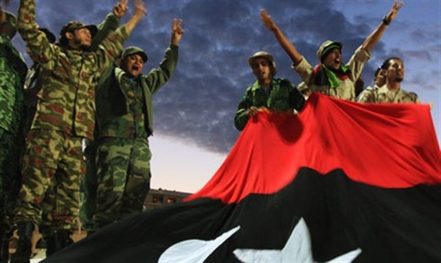[Anti-Qaddafi fighters gesture to the crowds in front of a Kingdom of Libya flag during celebrations in Benghazi on 23 October. Image by Esam Omran Al-Fetori/Reuters]