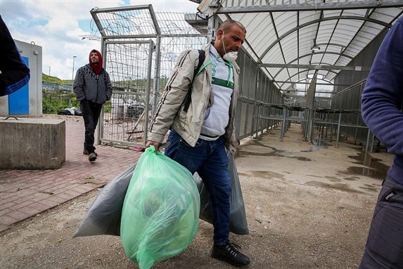 Palestinian workers from the West Bank city of Hebron carry personal belongings as they arrive to cross to Israel at a checkpoint in Tarqumiya, 18 March 2020 via Flash90 by Wisam Hashlamoun