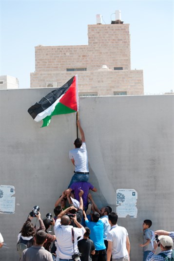 [Youth raise the Palestinian flag over the wall between the Israeli settlement Har Gilo and the West Bank town of Al-Walaja,16 September, 2011: Image from www.shutterstockcom]