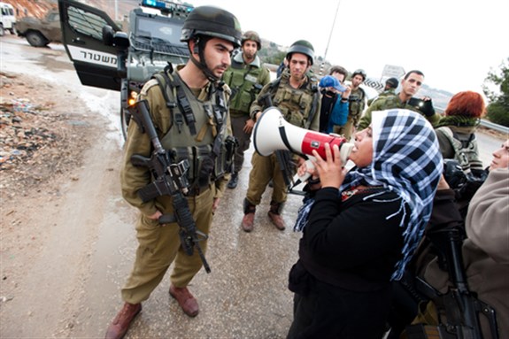 [An unidentified Palestinian confronts soldiers while protesting the Israeli separation wall surrounding her village of Al-Walaja, West Bank on Nov. 18, 2011: Image from www.shutterstockcom]