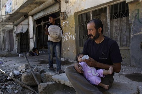 [A Syrian man feeds his daughter while sitting in front of his partly damaged house, in Azaz, on the outskirts of Aleppo, Syria, Aug. 28, 2012. Image by Muhammed Muheisen/AP Photo.]