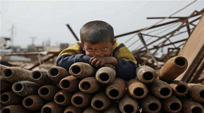 A Syrian child poses atop a stack of neutralized shells at a metal scrapyard on the outskirts of Maaret Misrin town in the northwestern Idlib province, on March 10, 2021. - AAREF WATAD/AFP via Getty Images