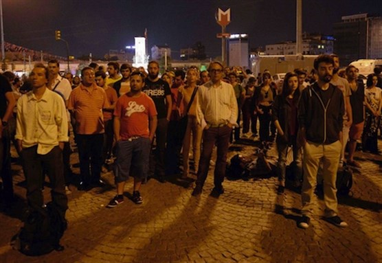 [Erdem Gunduz, left, and dozens of people stand silently in Taksim Square, 18 June 2013. Image from Associated Press.]